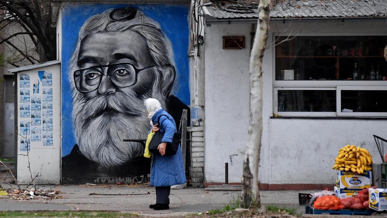 A woman walks past a graffiti representing former Bosnian Serb leader Radovan Karadzic (shown here as Doctor Dabic from the time he was in hiding) on the wall of a tavern in Belgrade on March 20, 2019. - Former Bosnian Serb leader Radovan Karadzic will spend the rest of his life in jail for the "sheer scale and systematic cruelty" of his crimes in the war that tore his country apart a quarter of a century ago, UN judges said on March 20, 2019. Karadzic, 73, stood motionless and grim-faced in the dock as judges in The Hague said they had upheld his 2016 convictions for genocide in the Srebrenica massacre and war crimes in the 1990s. (Photo by Andrej ISAKOVIC / AFP)