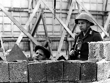 Das Archivbild von 1962 zeigt einen Soldaten der Nationalen Volksarmee, rechts, der einen Bauarbeiter bei der Reparatur der Berliner Mauer an der Bernauer Straße beaufsichtigt.