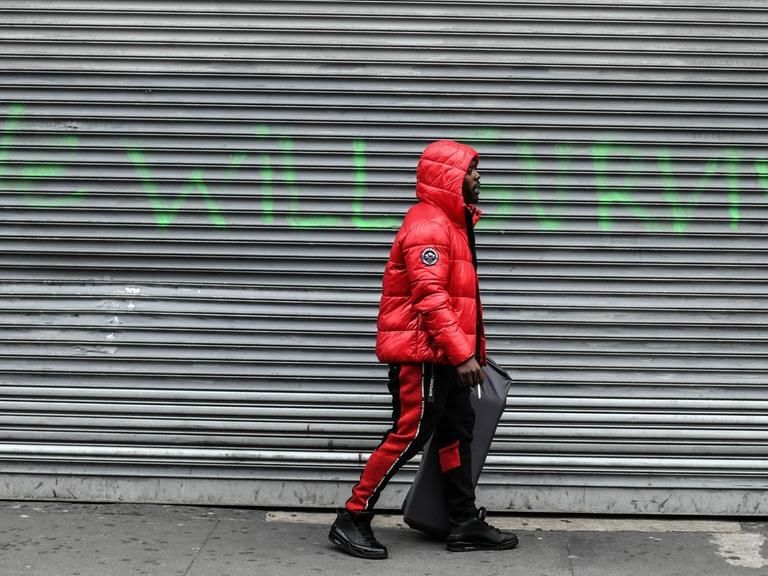 Ein Mann in der New Yorker Bronx läuft an einem geschlossenen Geschäft vorbei. Auf den Rolläden steht "We will survive", aufgenommen am 16. April 2020.