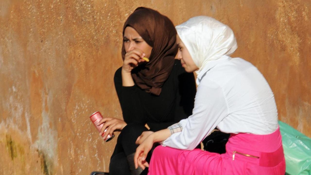 Zwei junge Frauen mit Kopftüchern und Gewändern sitzen auf einer Bank an einer Mauer in der Altstadt von Rabat, aufgenommen am 11.03.2015.