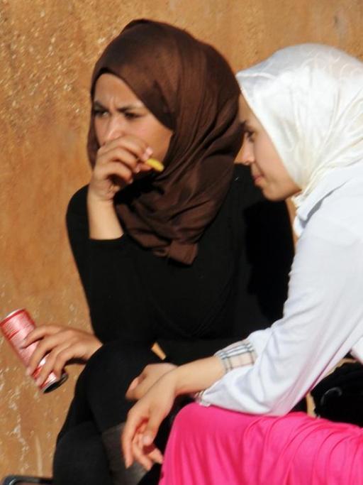 Zwei junge Frauen mit Kopftüchern und Gewändern sitzen auf einer Bank an einer Mauer in der Altstadt von Rabat, aufgenommen am 11.03.2015.