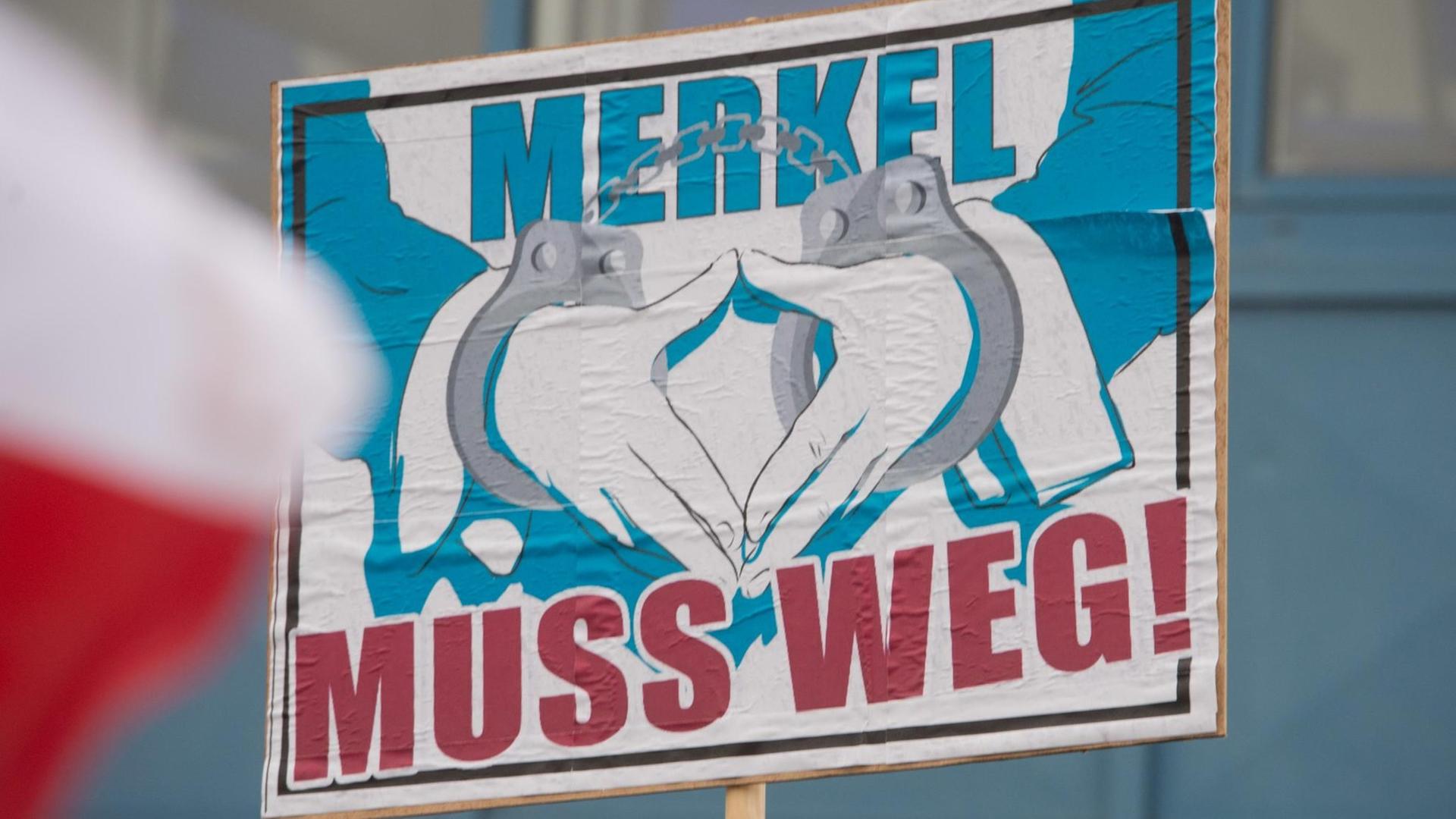 Ein Plakat mit der Aufschrift "Merkel muss weg" und eine mit zwei Händen geformte Raute