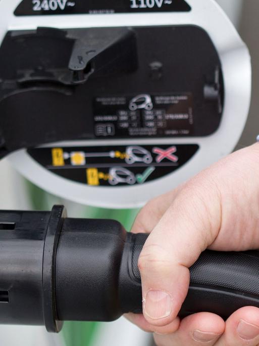 Ein Autofahrer steckt einen Ladestecker einer E-Mobilität-Zapfsäule in ein batteriebetriebenes Fahrzeug.