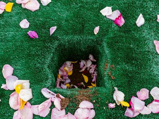 Ein Urnengab, ausgelegt mit grünem Kunstrasen und dekoriert mit Blütenblättern.