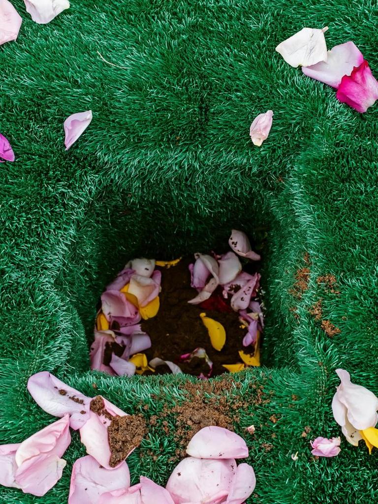 Ein Urnengab, ausgelegt mit grünem Kunstrasen und dekoriert mit Blütenblättern.