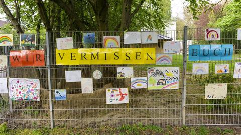 Am Zaun eines Kindergartens hängen Bilder und ein Schild mit der Aufschrift: Wir vermissen euch.