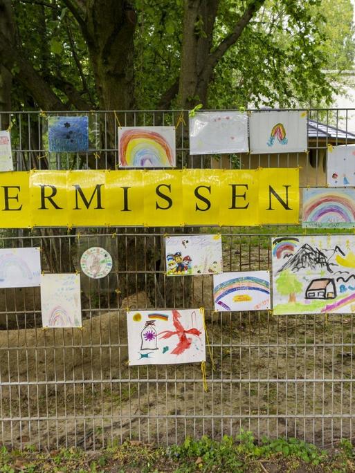 Am Zaun eines Kindergartens hängen Bilder und ein Schild mit der Aufschrift: Wir vermissen euch.