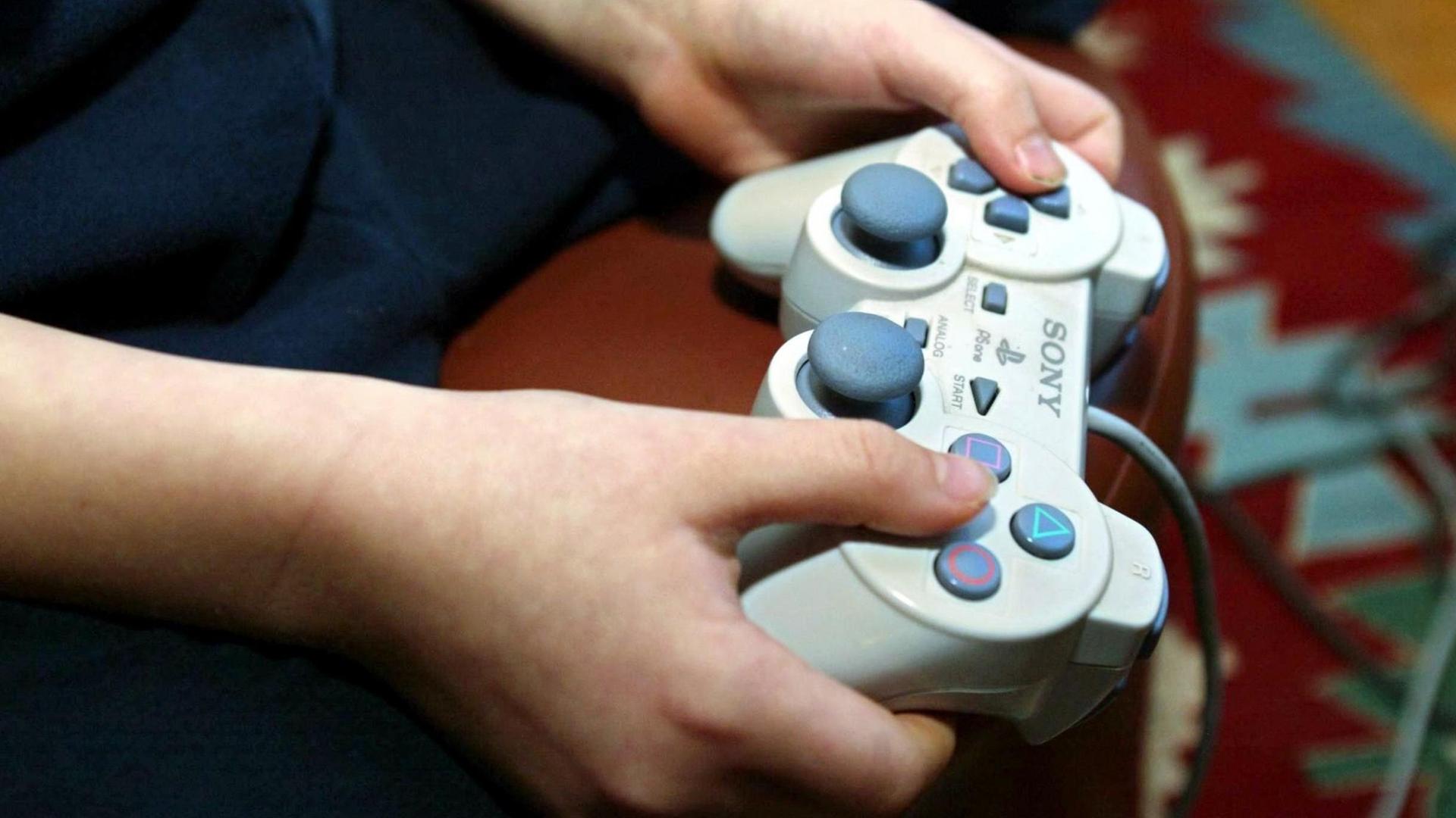 Ein Junge sitzt im Wohnzimmer und spielt ein Playstation-Videospiel mit der typischen Spielekonsole.
