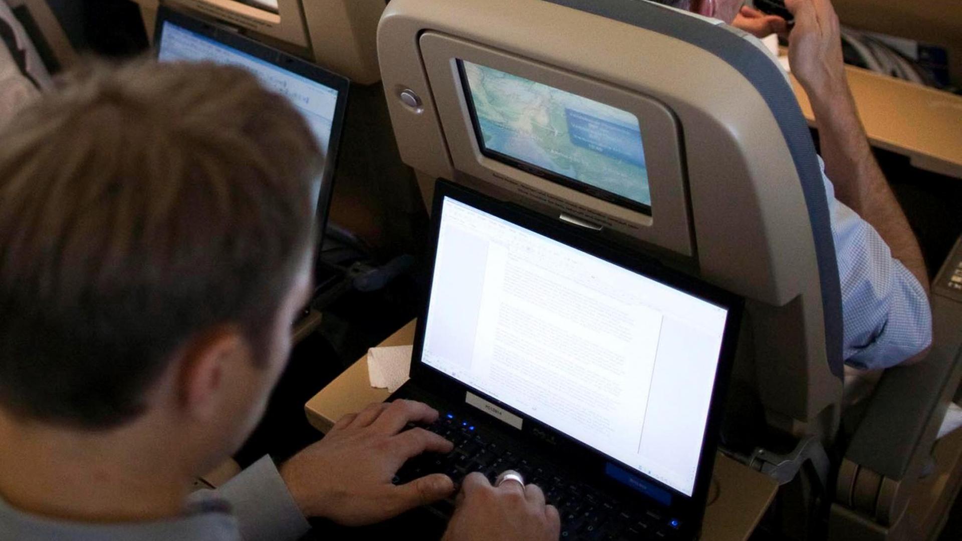 Ein Mann blickt in einem Flugzeug auf einen Laptop.