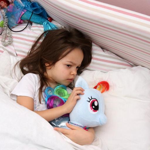 Ein kleines Maedchen liegt in einem Kinderzimmer und kuschelt mit ihrem Plüschtier (gestellte Szene).