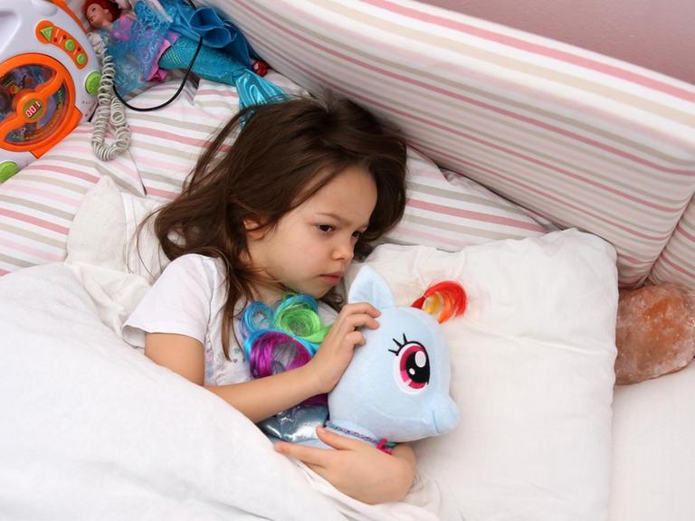 Ein kleines Maedchen liegt in einem Kinderzimmer und kuschelt mit ihrem Plüschtier (gestellte Szene).