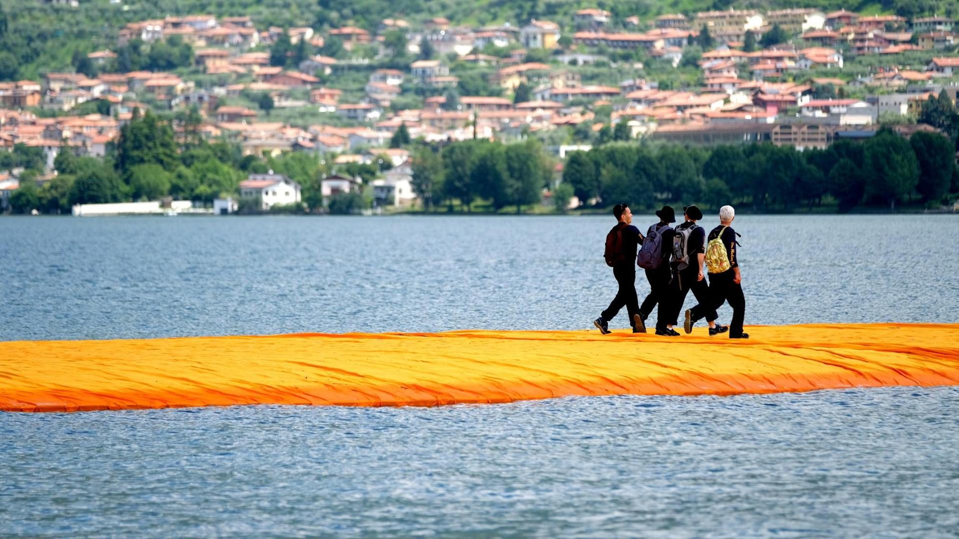 Menschen gehen am 17.06.2016 über orangefarbene, schwimmenden Stege im Rahmen des Projekts "The Floating Piers" von Christo auf dem Lago d'Iseo in Italien.