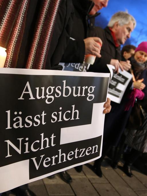 "Augsburg lässt sich Nicht Verhetzen" steht auf dem Plakat eines Mannes der am Königsplatz bei der Kranzniederlegung eines AfD-Abgeordneten gegen politische Instrumentalisierung demonstriert.