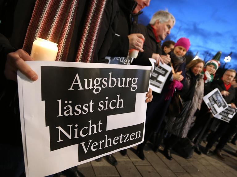 "Augsburg lässt sich Nicht Verhetzen" steht auf dem Plakat eines Mannes der am Königsplatz bei der Kranzniederlegung eines AfD-Abgeordneten gegen politische Instrumentalisierung demonstriert.