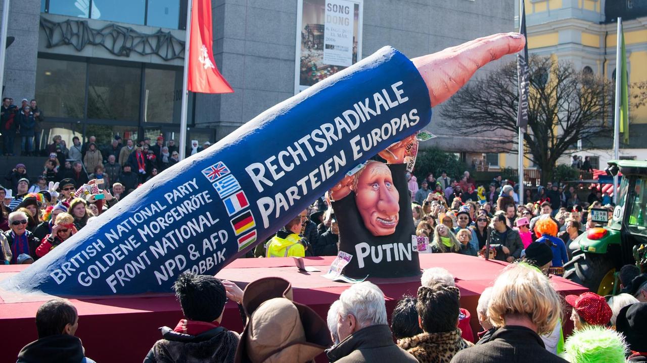 Ein Mottowagen vom Düsseldorfer Umzug: Der russische Präsident Putin stützt einen rechten ausgestreckten Arm. Auf dem Arm stehen die Namen von nationalistischen europäischen Gruppierungen. Ein Mottowagen vom Düsseldorfer Umzug: Der russische Präsident Putin stützt einen rechten ausgestreckten Arm. Auf dem Arm stehen die Namen von nationalistischen europäischen Gruppierungen.