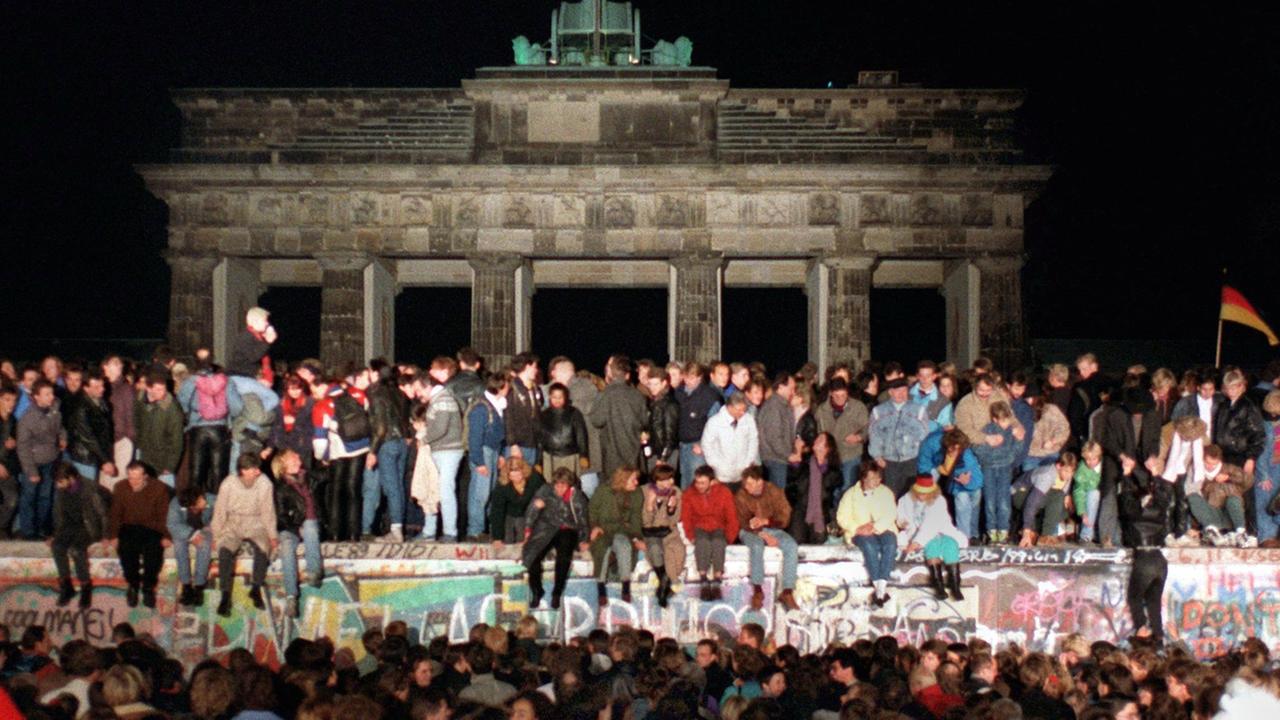 Jubelnde Menschen auf der Berliner Mauer am Brandenburger Tor. 