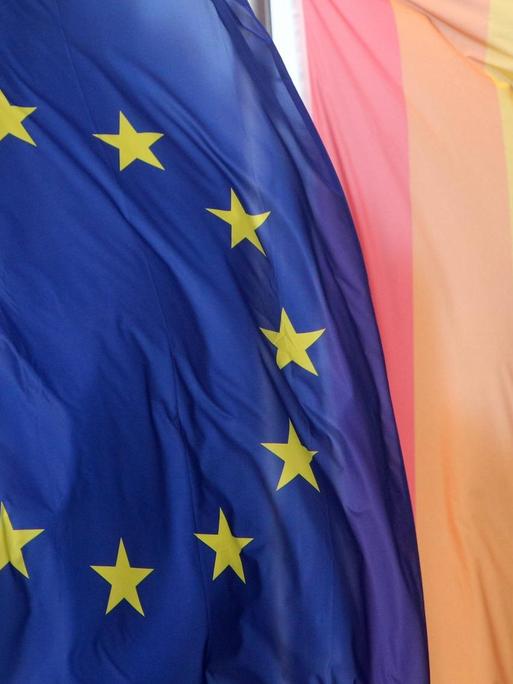 Eine Flagge der Europäischen Union weht neben einer Regenbogenflagge.