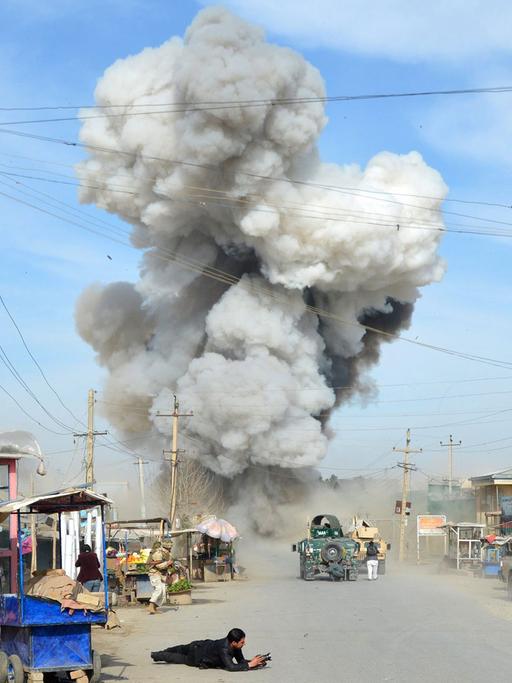 Nach einem Selbstmord-Bombenanschlag durch fünf Talibankämpfer auf ein Polizei-Hauptquartier in Kundus in Afghanistan am 10.02.2015 steigt über einer Straße mit Militärfahrzeugen eine Rauchwolke auf.