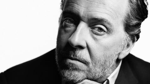 Christian Gerhaher stützt seinen Kopf auf die Hände, blickt hinterfragend.