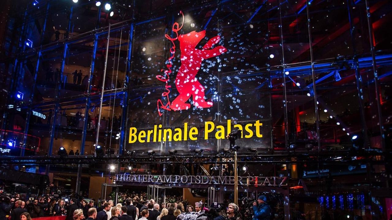 Der Berlinale-Palast am Abend, mit dem roten Bären an der Glasfront, davor viele Menschen auf und neben dem roten Teppich  