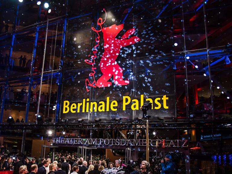 Der Berlinale-Palast am Abend, mit dem roten Bären an der Glasfront, davor viele Menschen auf und neben dem roten Teppich  