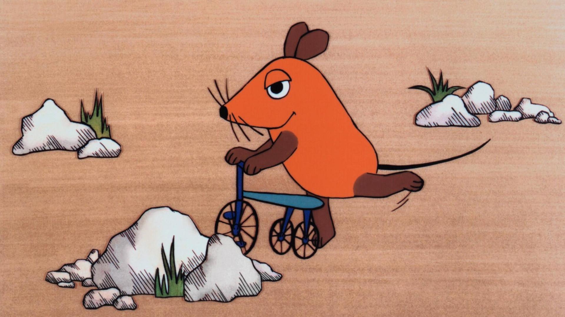 Ein Farbfoto zeigt die orangefarbene, offenbar erfreute Zeichentrick-Maus auf einem blauen Roller, umgeben von einigen weißen Felsen und kargen Grasbüscheln. Die erste Folge der "Sendung mit der Maus", ausgestrahlt am 7. März 1971 The Mouse Television: Die Sendung Mit Der Maus The Broadcast With The Mouse TV-Serie De 1971-, 07 March 1971 PUBLICATIONxINxGERxSUIxAUTxONLY Copyright: WdrxAFxArchivexMaryxEvans 12452915 editorial use only