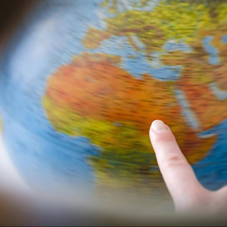 Eine Frau tippt mit dem Finger an einen Globus der sich dreht