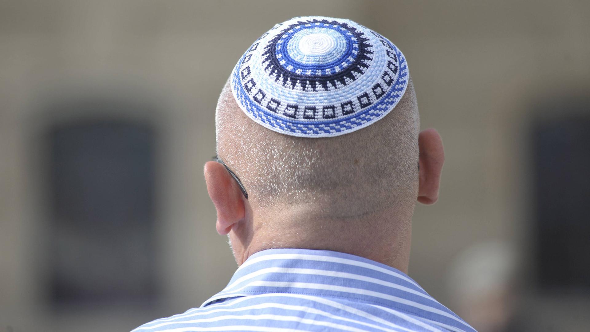 Ein Mann mit kurzen Haaren und einem blau-weiß gestreiften Hemd trägt eine blau-weiße Kippa in Berlin.