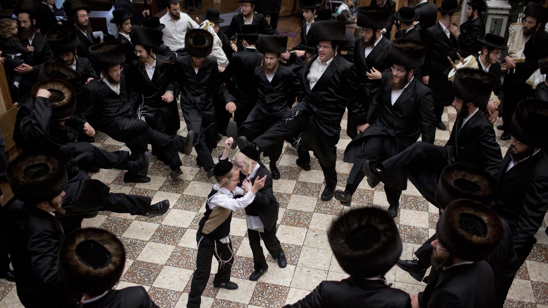Jüdische Männer tanzen in einem Kreis, in der Mitte stehen zwei kleine Jungen.