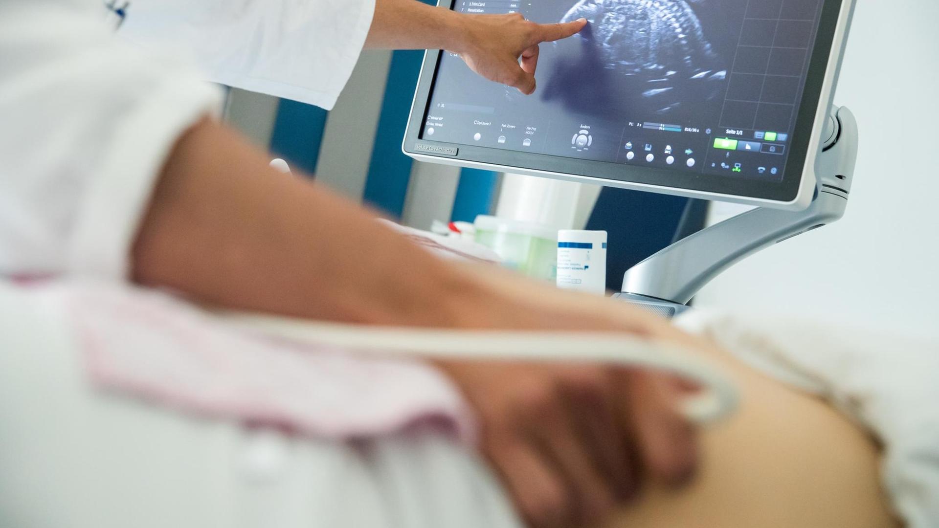Ein Arzt untersucht eine schwangere Frau mit Ultraschall und zeigt ihr etwas auf dem Bildschirm.