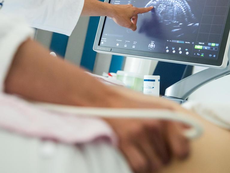 Ein Arzt untersucht den Bauch von einer Frau mit einem Ultraschall-Gerät