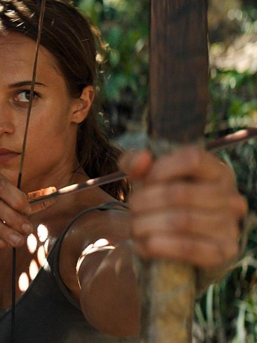 Alicia Vikander als Lara Croft in "Tomb Raider", sie ist von vorne zu sehen, schaut konzentriert und spannt einen Bogen