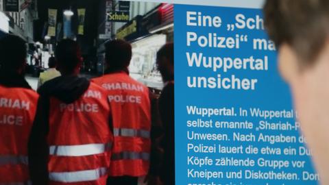 Ein Mann blickt auf einen Computer-Bildschirm, auf dem selbsternannte "Scharia-Polizisten" zu sehen sind.