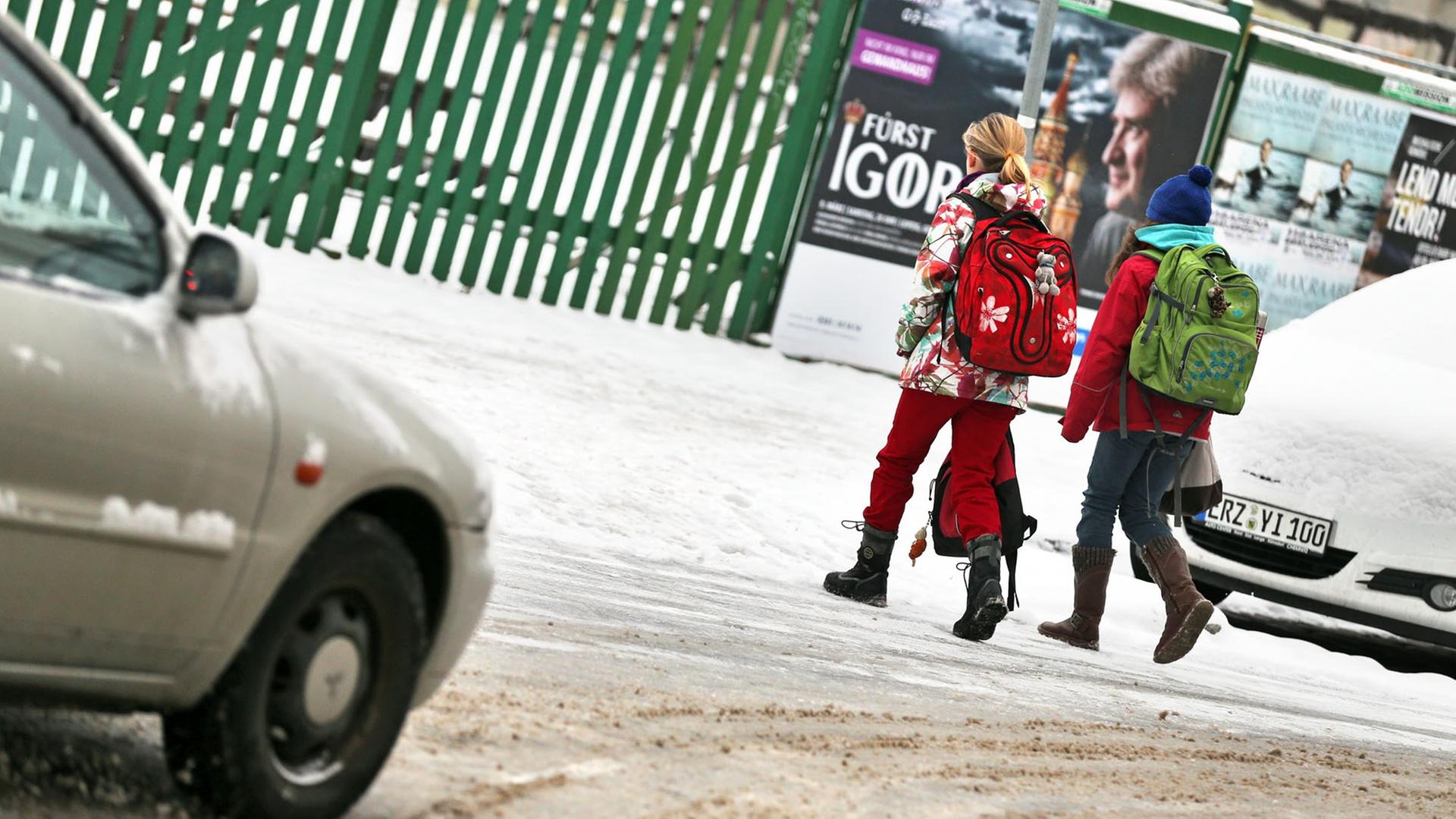 Zwei Schulkinder gehen über eine verschneite Straße in Leipzig (Sachsen).