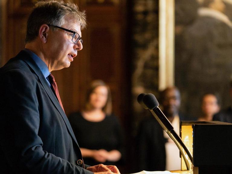 Der Historiker Jürgen Zimmerer steht hinter einem Rednerpult und hält eine Ansprache.