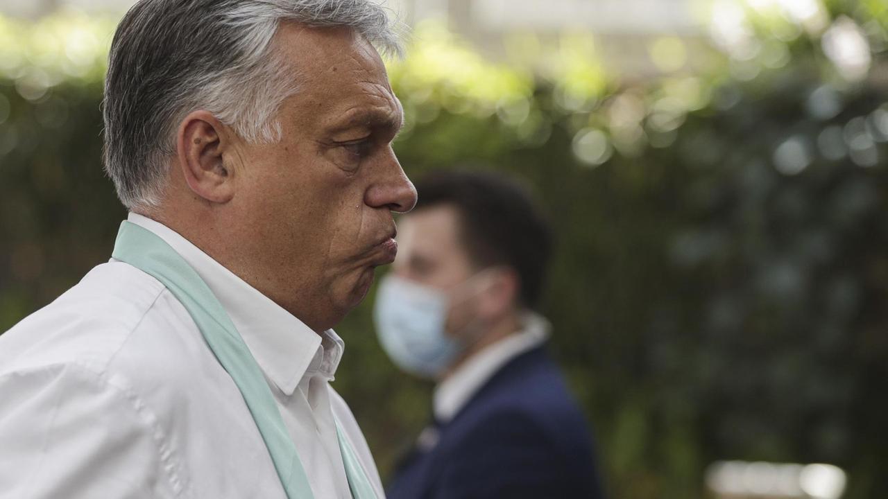 Zu sehen ist Viktor Orban, Premierminister von Ungarn. Im Hintergrund ein Mann mit Mund-Nasen-Bedeckung.