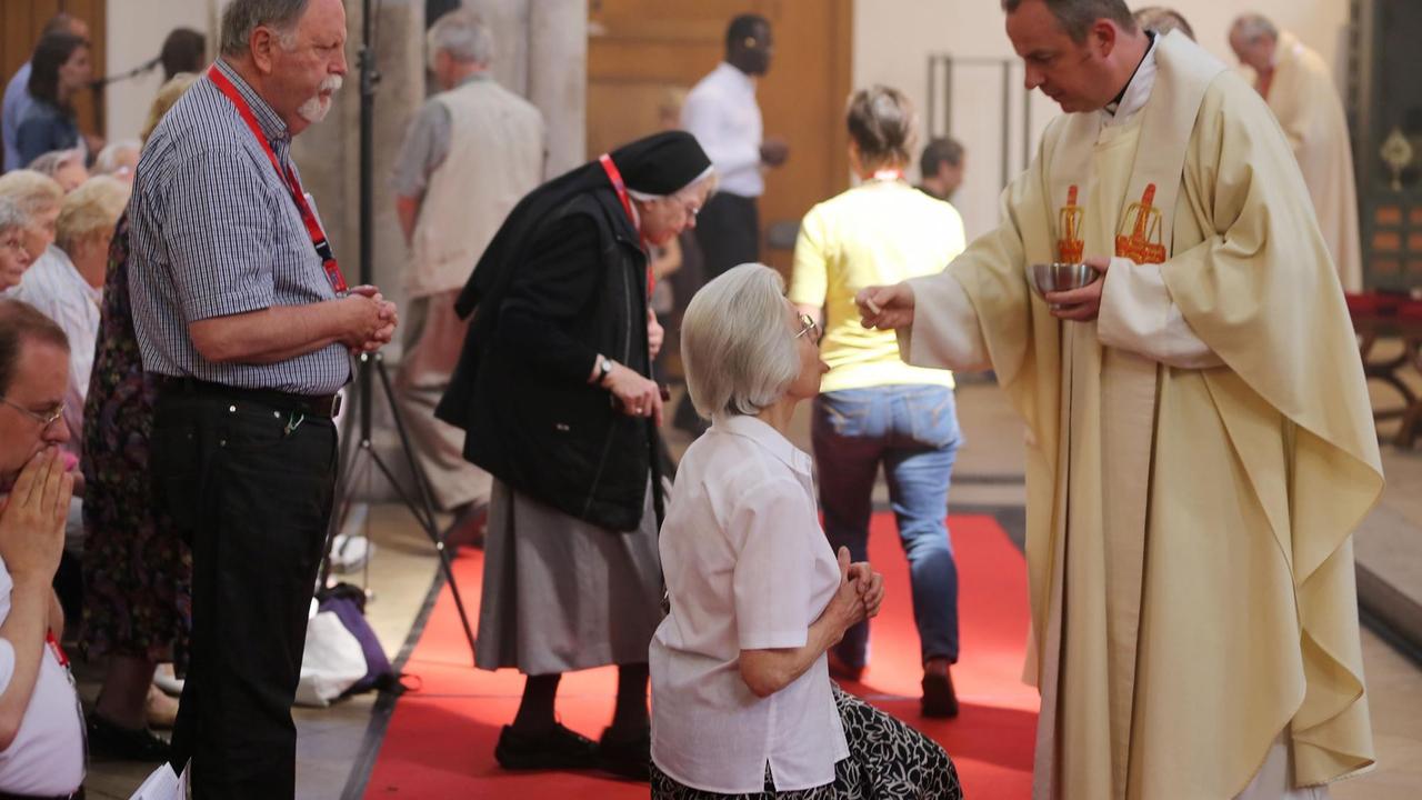 Gläubige nehmen am 07.06.2013 in Köln (Nordrhein-Westfalen) an einer Eucharistiefeier teil. Der Priester legt einer knienden Dame eine Hostie auf ihre Zunge