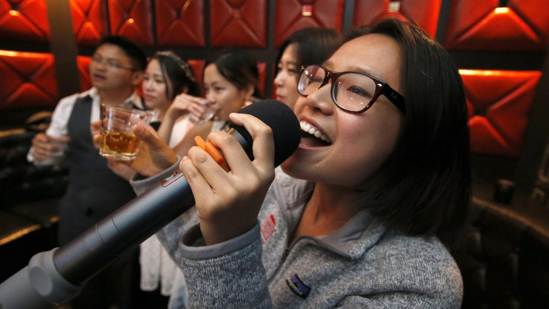 Eine Frau singt mit weiteren Gästen in einer Karaoke-Bar