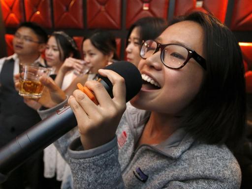 Eine Frau singt mit weiteren Gästen in einer Karaoke-Bar