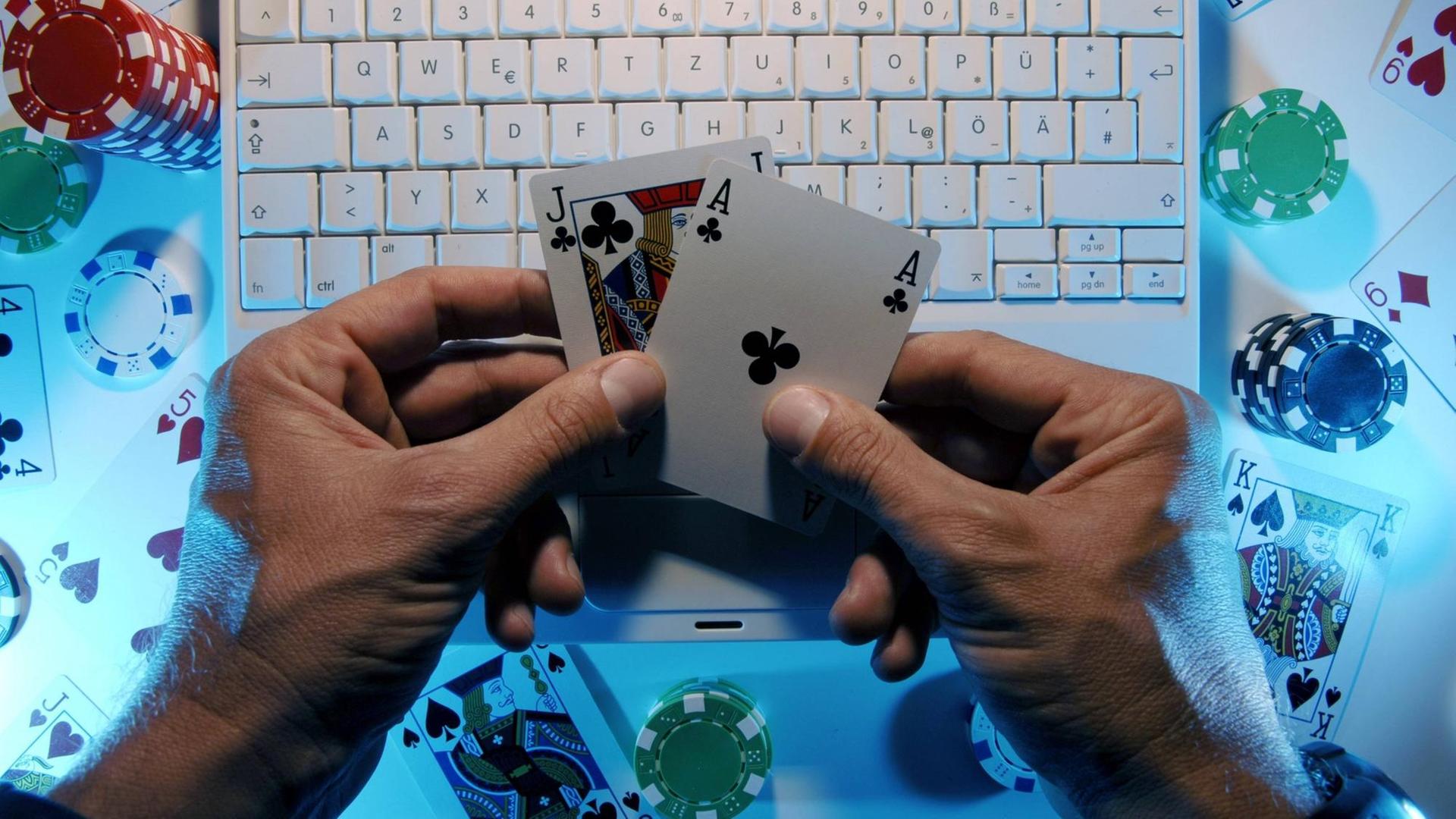Hände eines Onlinepokerspielers halten ein Buben und ein Ass vor einer Computertastatur.