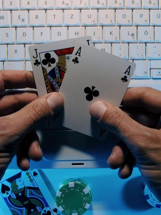 Hände eines Onlinepokerspielers halten ein Buben und ein Ass vor einer Computertastatur.