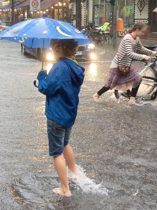 Kinder gehen am 29. Juni 2017 in Berlin auf einer überfluteten Straße im Stadtteil Schöneberg über eine Kreuzung.