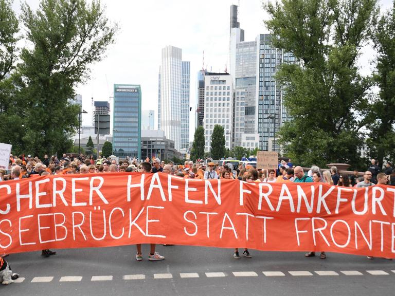 Demonstranten halten vor der Banken-Kulisse der Stadt ein Transparent mit der Aufschrift "Sicherer Hafen Frankfurt - Seebrücke statt Frontex" hoch.