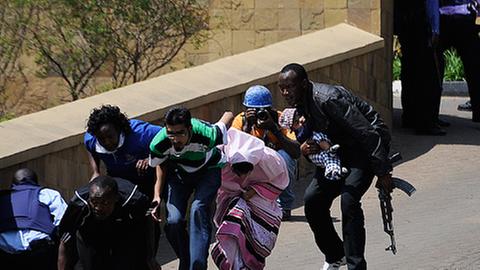 Auf einem Zugangsweg fliehen mehrere Menschen aus dem Westgate-Einkaufszentrum in Nairobi, sie laufen geduckt hinter einer Mauer.