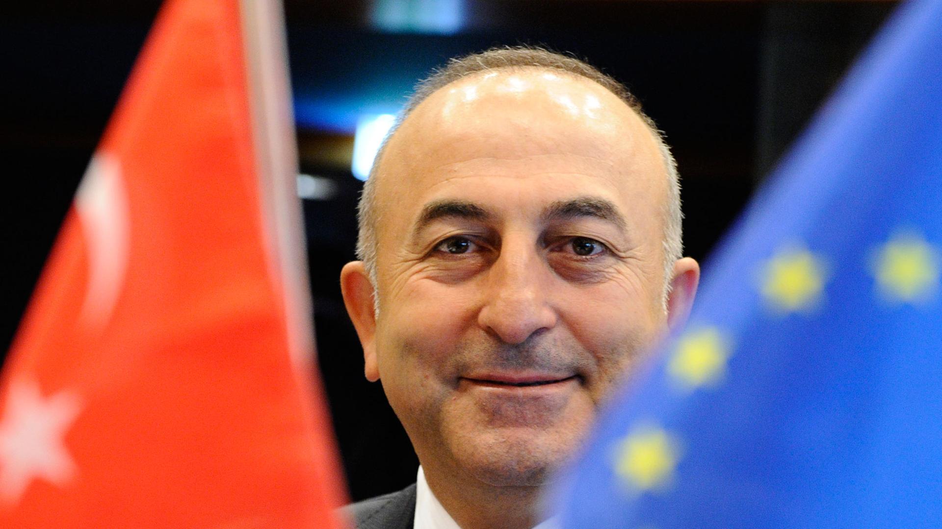 Der neue türkische Außenminister Mevlut Cavusoglu lächelt am 23.06.2014 zwischen einer Türkei- und einer EU-Flagge, kurz vor Beginn eines Treffens des EU-Türkei-Assoziierungsrates in Luxemburg.