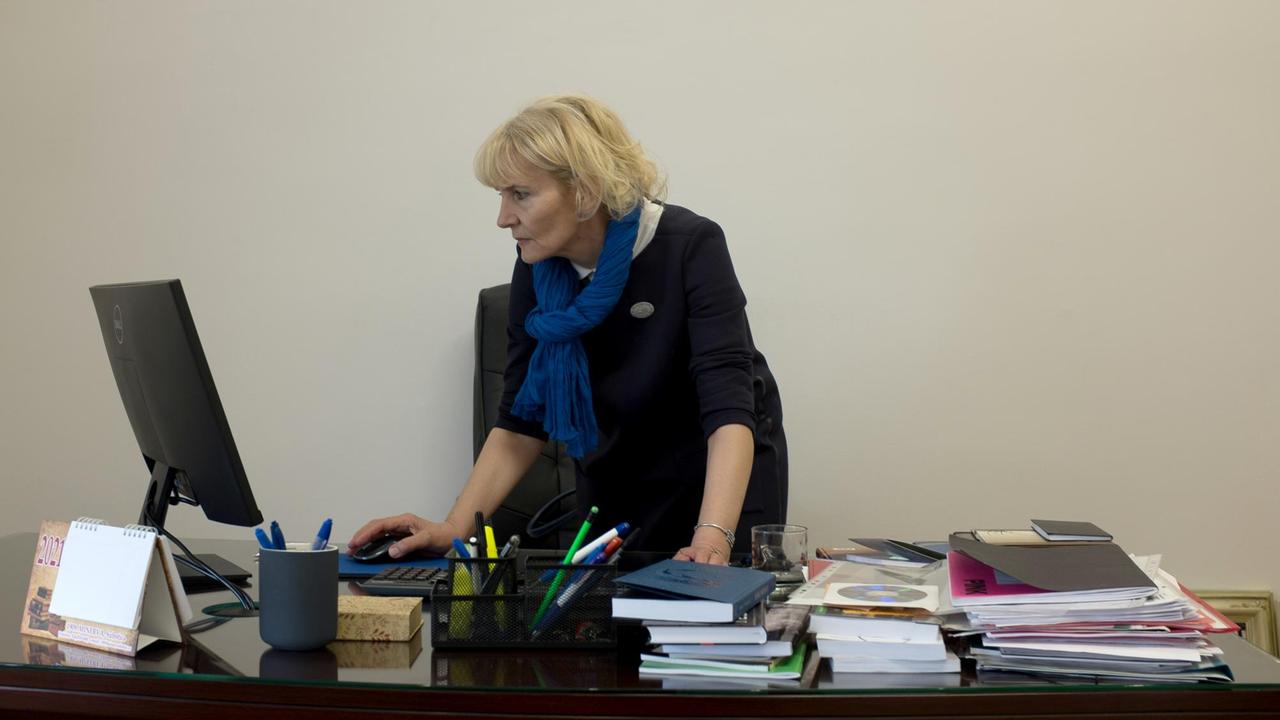 Bora Babic steht an ihrem Schreibtisch auf dem viele Bücher und Papier legen und ein Computerbildschirm steht