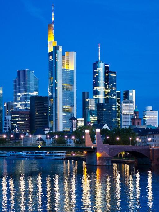 Im ersten Licht des Tages spiegeln sich am 26.08.2015 die Lichter der Skyline von Frankfurt am Main (Hessen) zur morgentlichen blauen Stunde im Fluss.