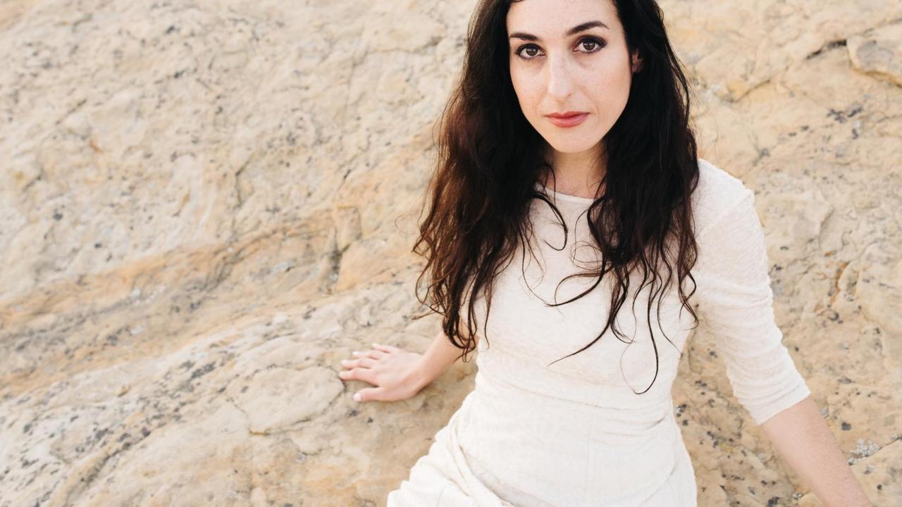 Marrissa Nadler sitzt auf beigen Steinen in einem weißen Kleid. Marrissa Nadler sitzt auf beigen Steinen in einem weißen Kleid.
