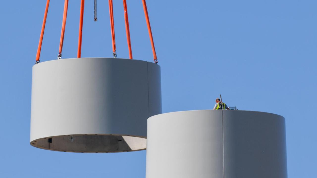 Ein weiteres Stahlsegment wird mit Hilfe eines Krans auf den Turm einer neuen Windenergieanlage gesetzt. 