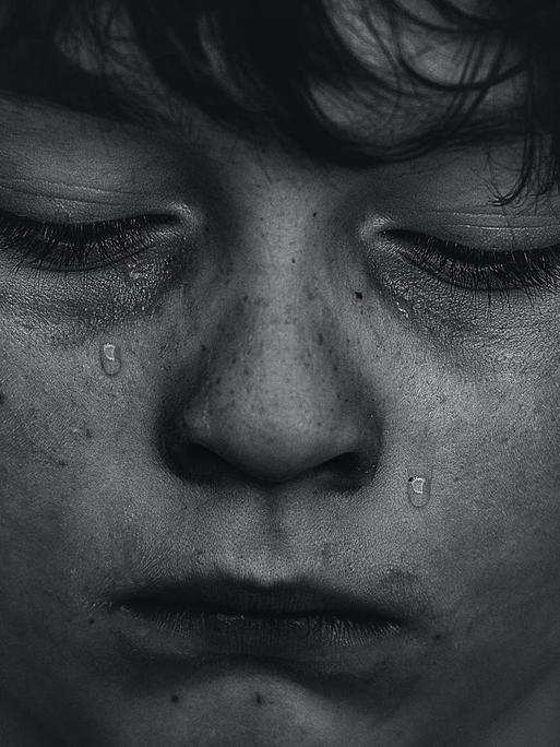 Schwarz-Weiß-Aufnahme eines Jungen, dem Tränen über das Gesicht laufen